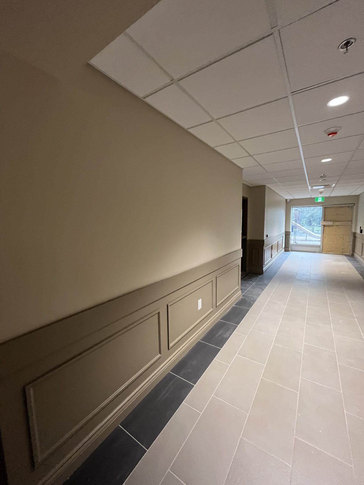 Corridor with beige painted walls, painted panel wainscoting and a white drop ceiling at 40 Polonia in Brampton