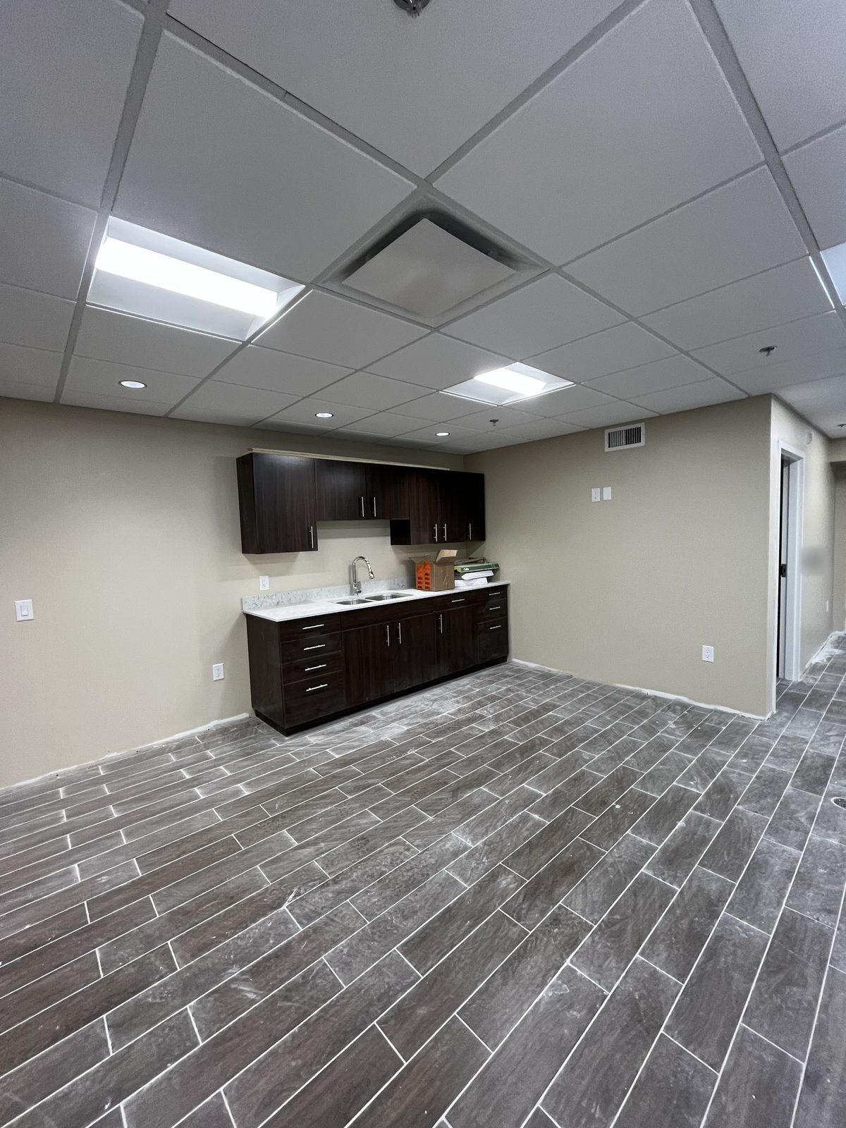 Room with beige painted walls, dark wood kitchenette cabinets and grey plank tile floor at 40 Polonia in Brampton