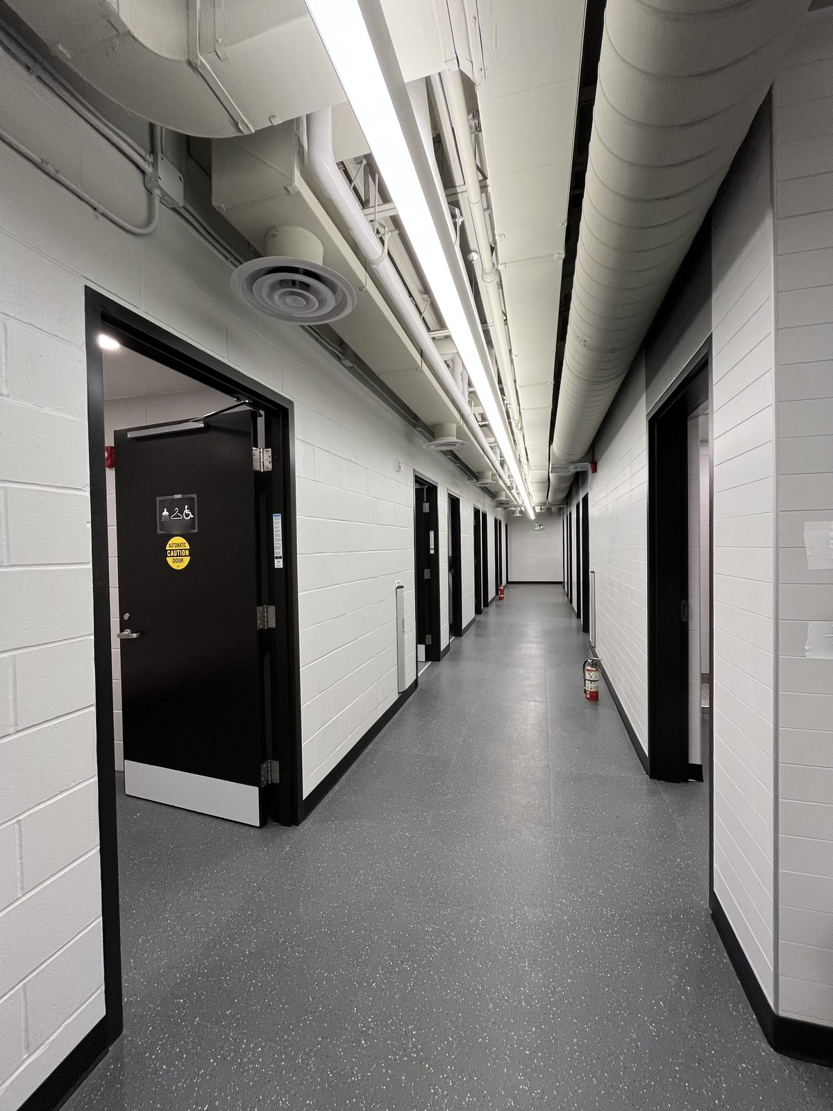Change room corridor with white painted block walls, black door frames and white exposed ductwork at the Albert McCormick Community Centre in Waterloo