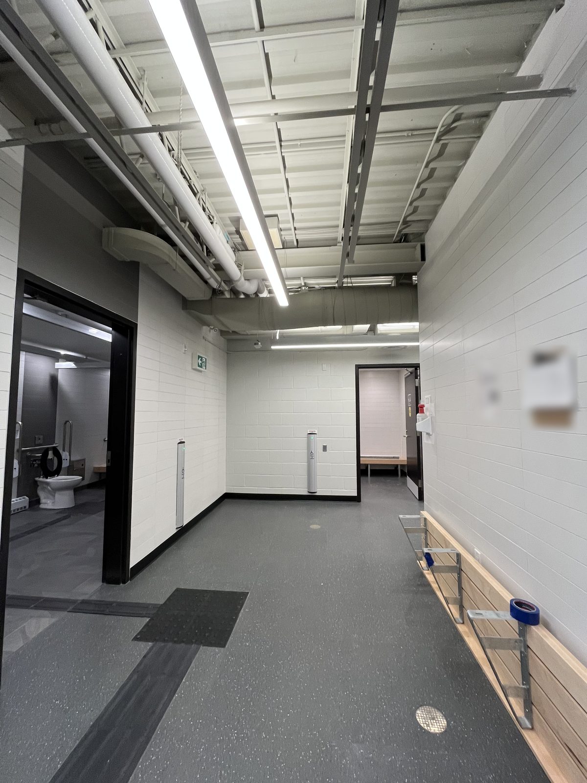 Change room entry area with white painted block walls, a white exposed ceiling and a wood bench at the Albert McCormick Community Centre in Waterloo