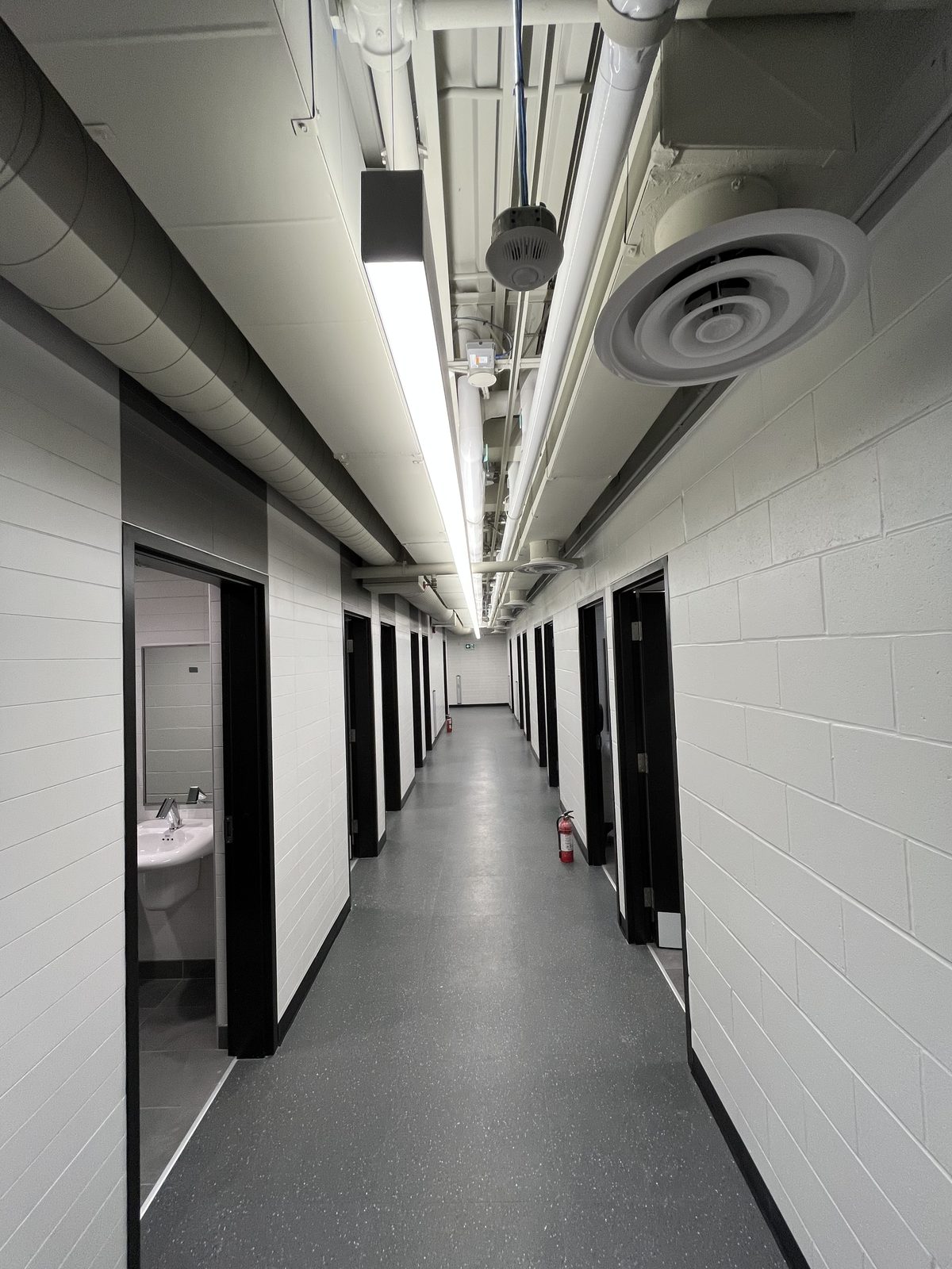 Long hallway of white painted block walls and black-framed change room doors under white exposed ductwork at the Albert McCormick Community Centre in Waterloo