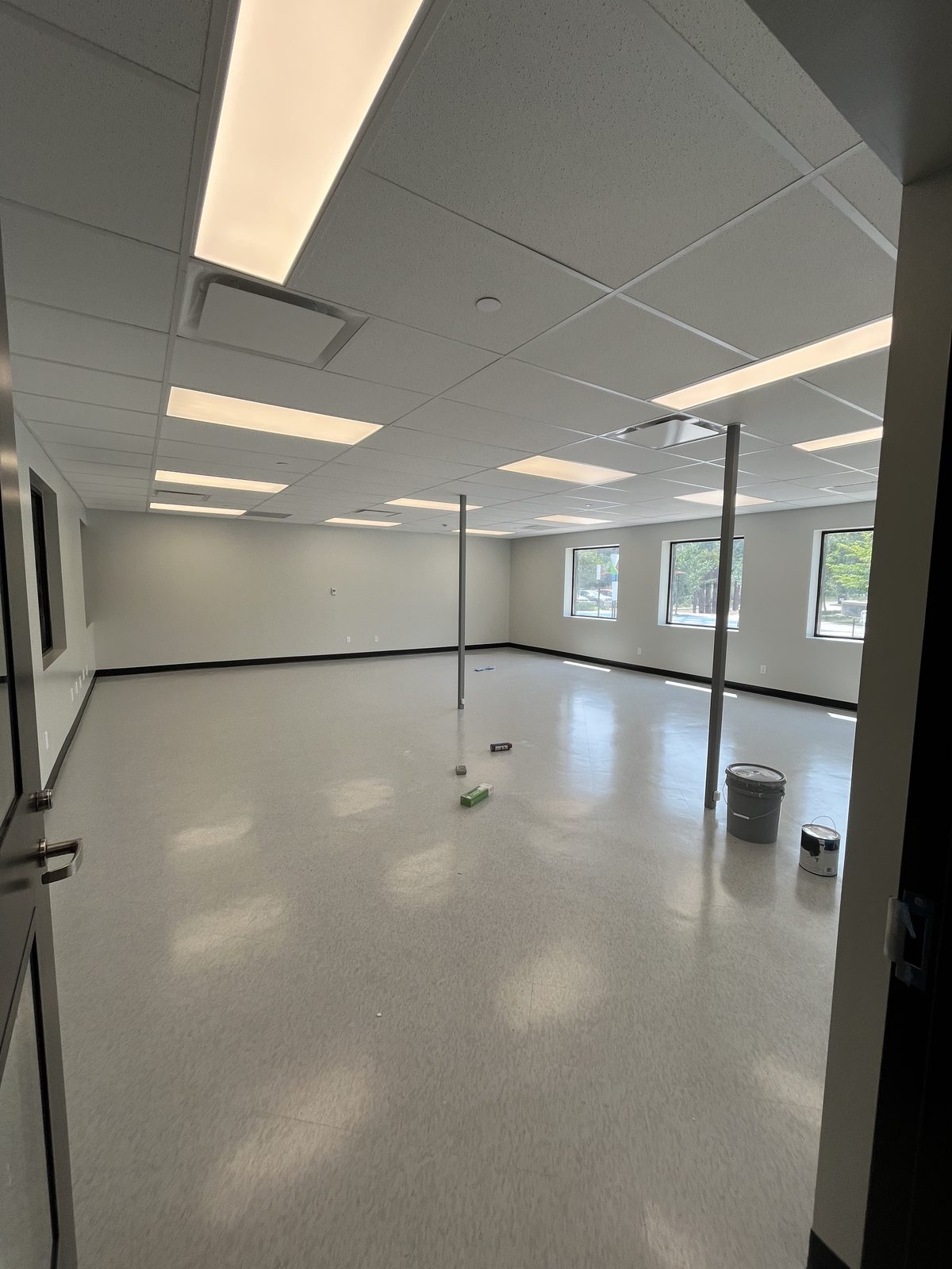 Bright multipurpose room with light grey painted walls, black base, a drop ceiling and three exterior windows at the Albert McCormick Community Centre in Waterloo