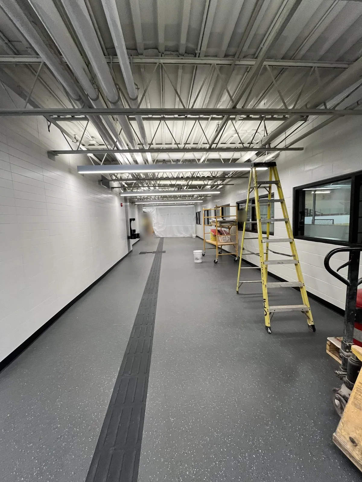Rink-side corridor with white painted block walls, white exposed steel joists and viewing windows, with scaffolding and a ladder in place at the Albert McCormick Community Centre in Waterloo