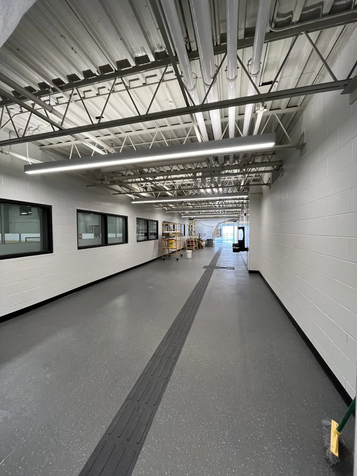 Corridor with white painted block walls, black-framed viewing windows, a white exposed ceiling and a tactile walking strip at the Albert McCormick Community Centre in Waterloo