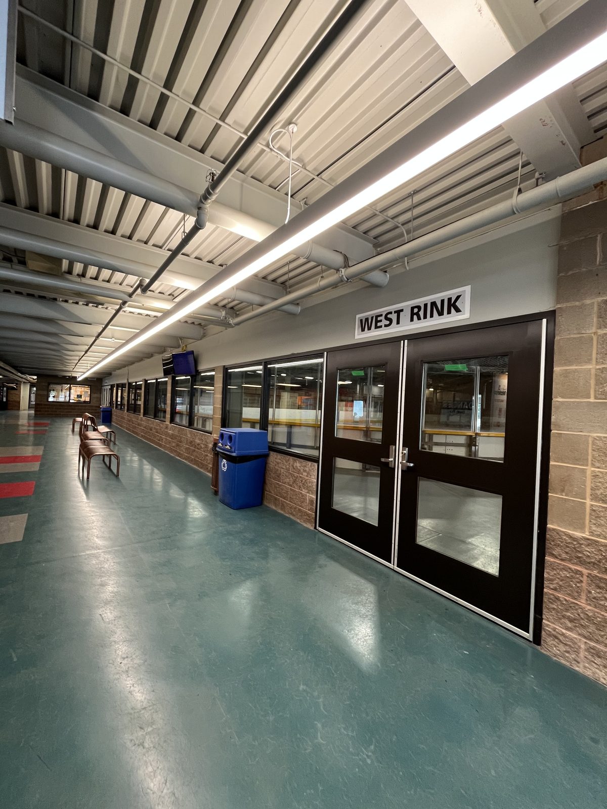 West Rink entrance with black-framed glass doors and a painted upper wall along the lobby corridor at the Albert McCormick Community Centre in Waterloo