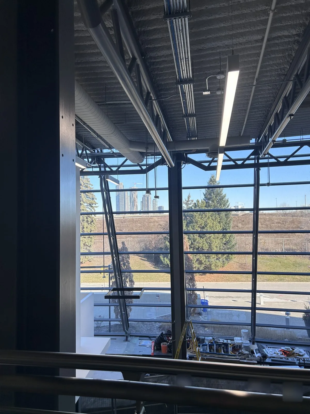 Atrium glazing and exposed ceiling seen from the mezzanine, with painting supplies and a ladder on the floor below