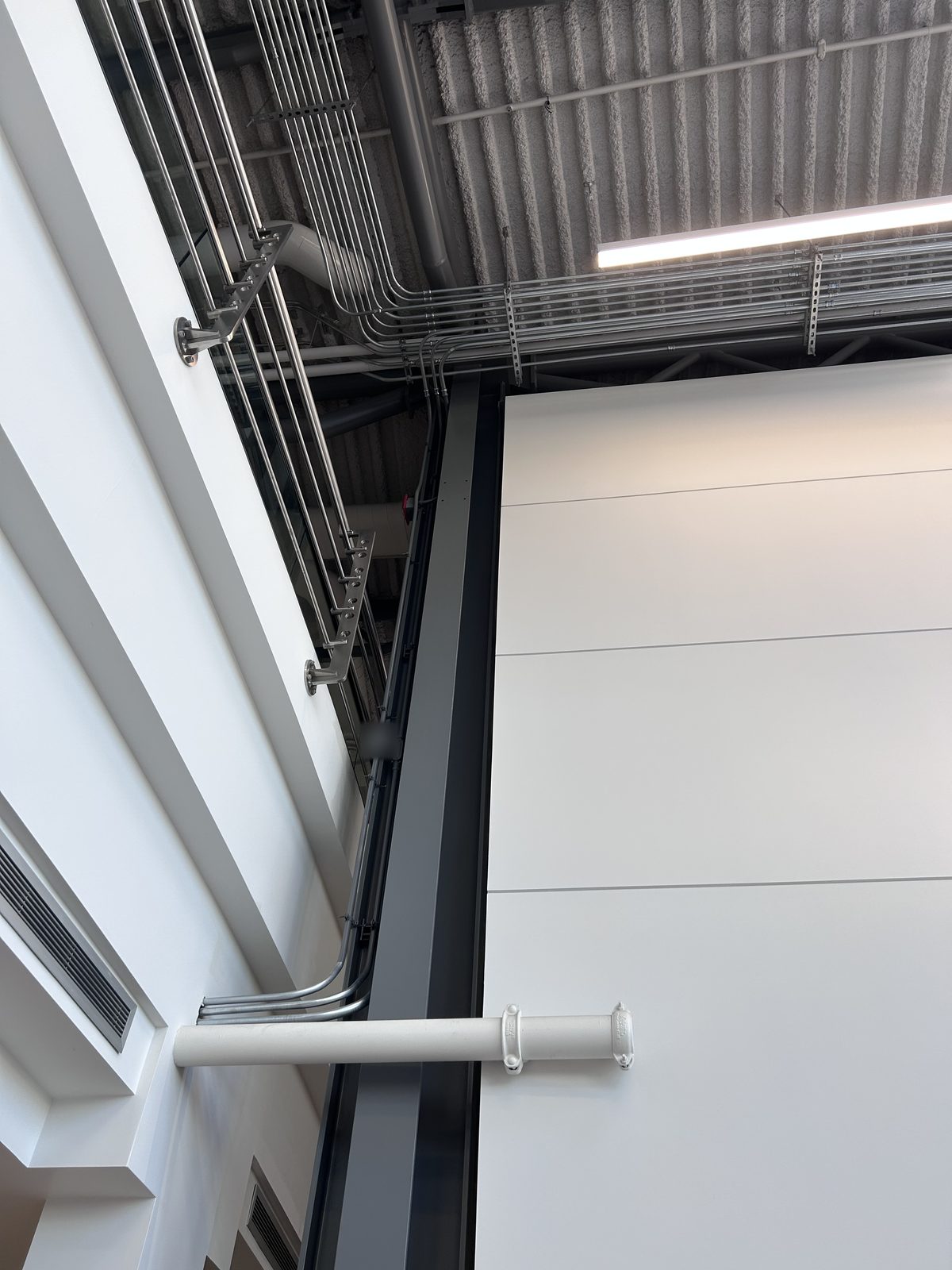 Exposed ceiling with conduit runs above a white painted panel wall and a dark grey steel column
