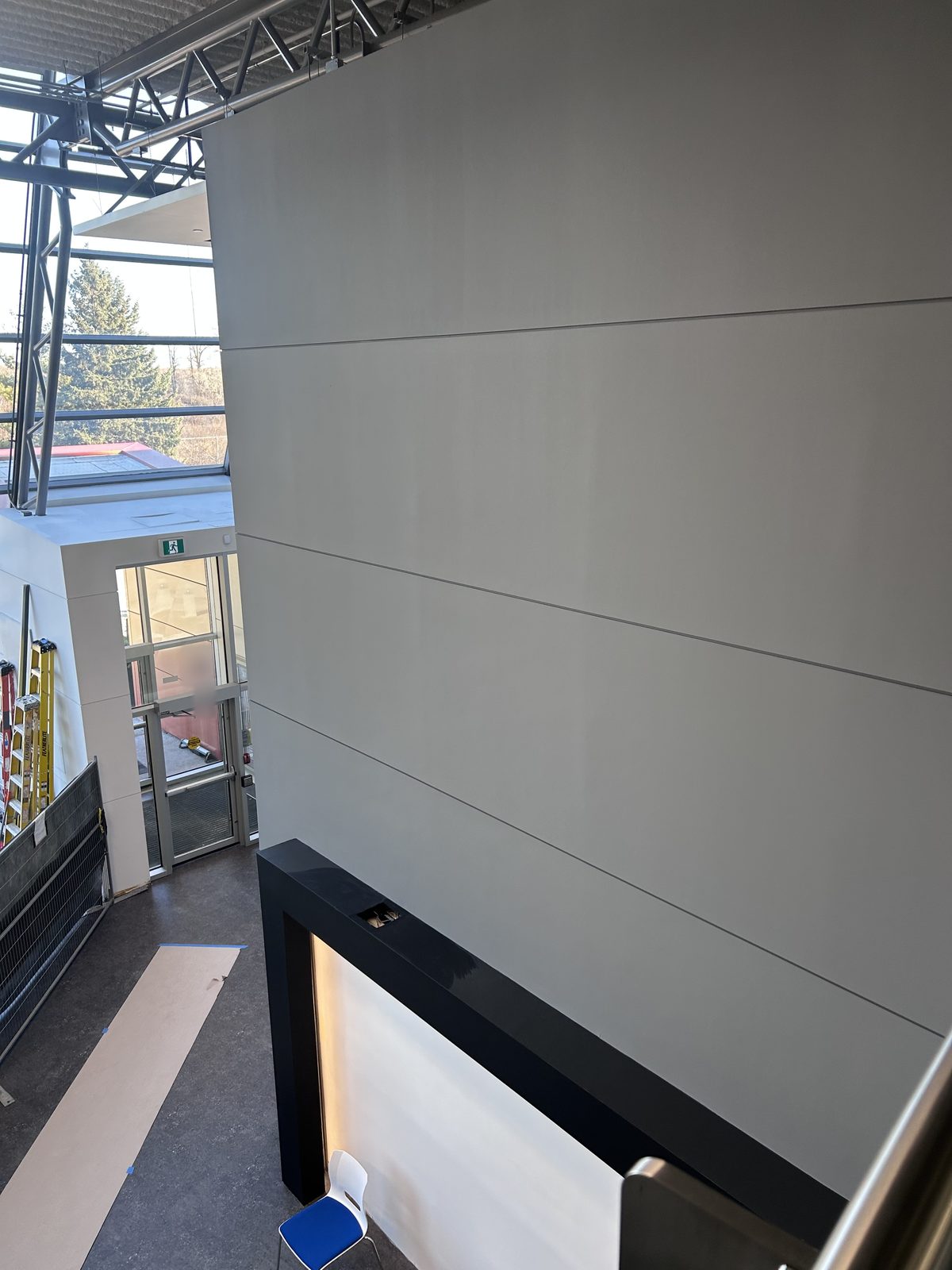 Grey painted feature wall and dark frame seen from above, with ladders and floor protection near the entrance