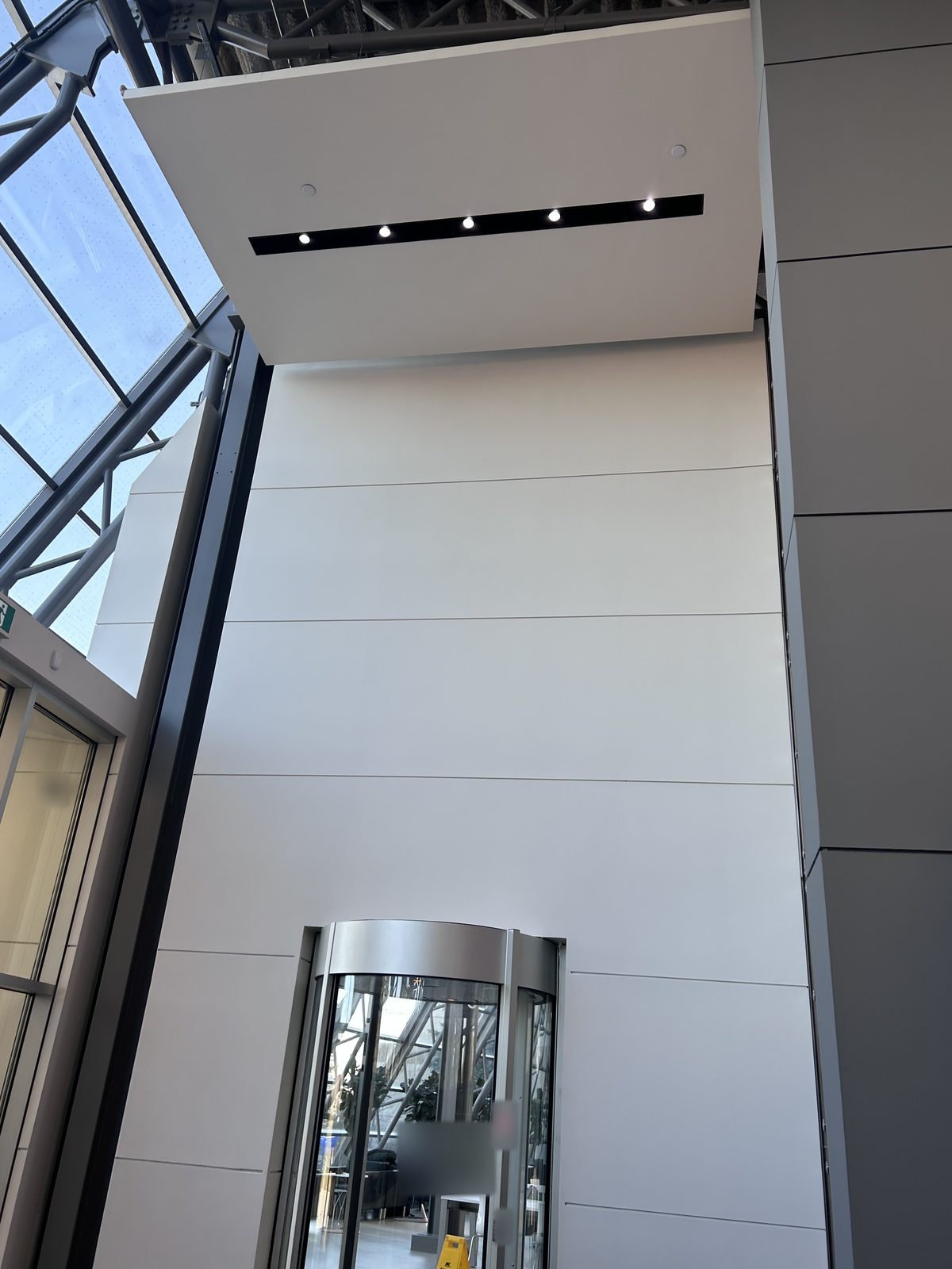 White painted feature wall with a soffit of recessed lights above a curved revolving door