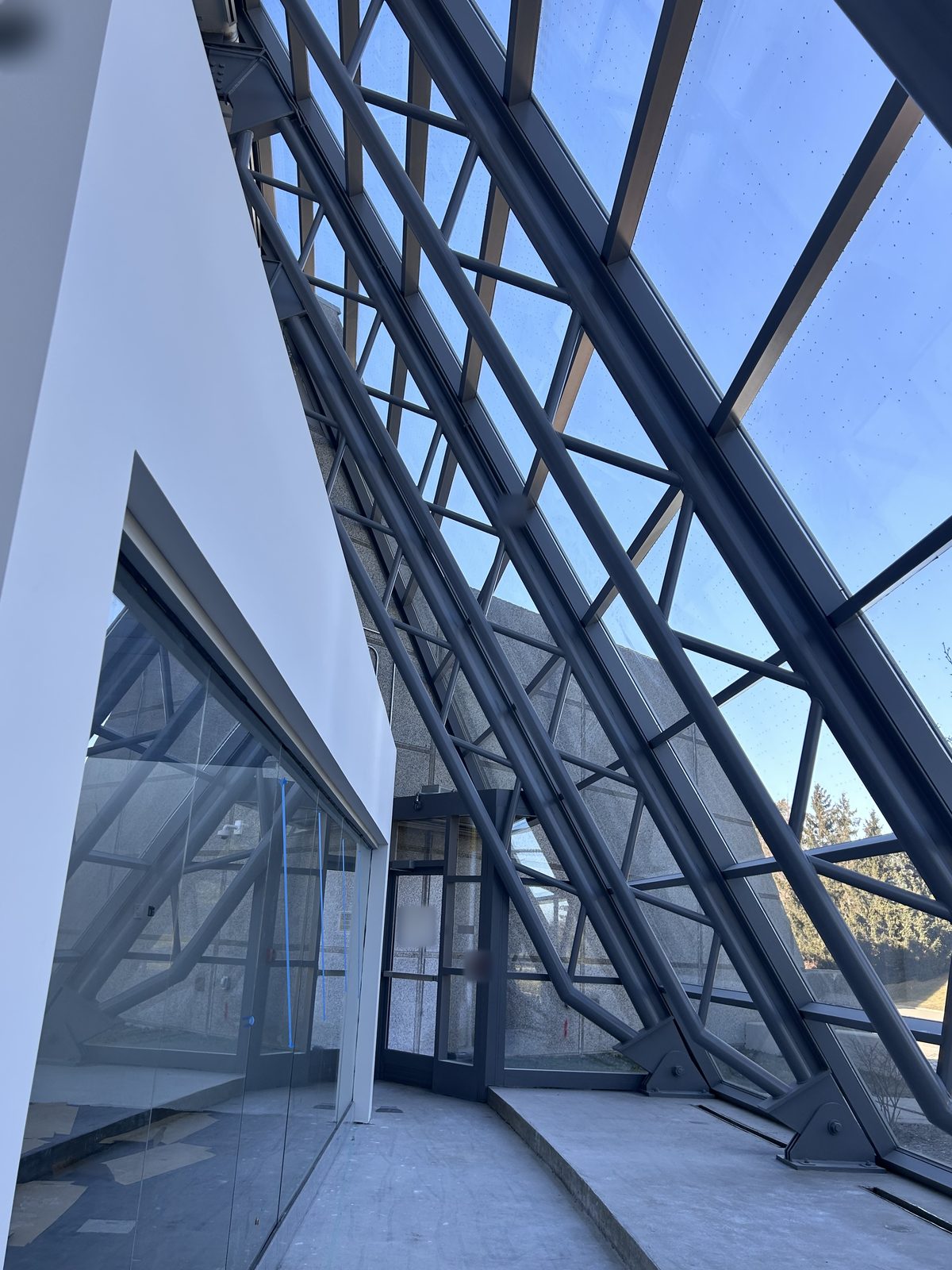 Glazed entrance vestibule with sloped steel-framed glass and floor protection in place