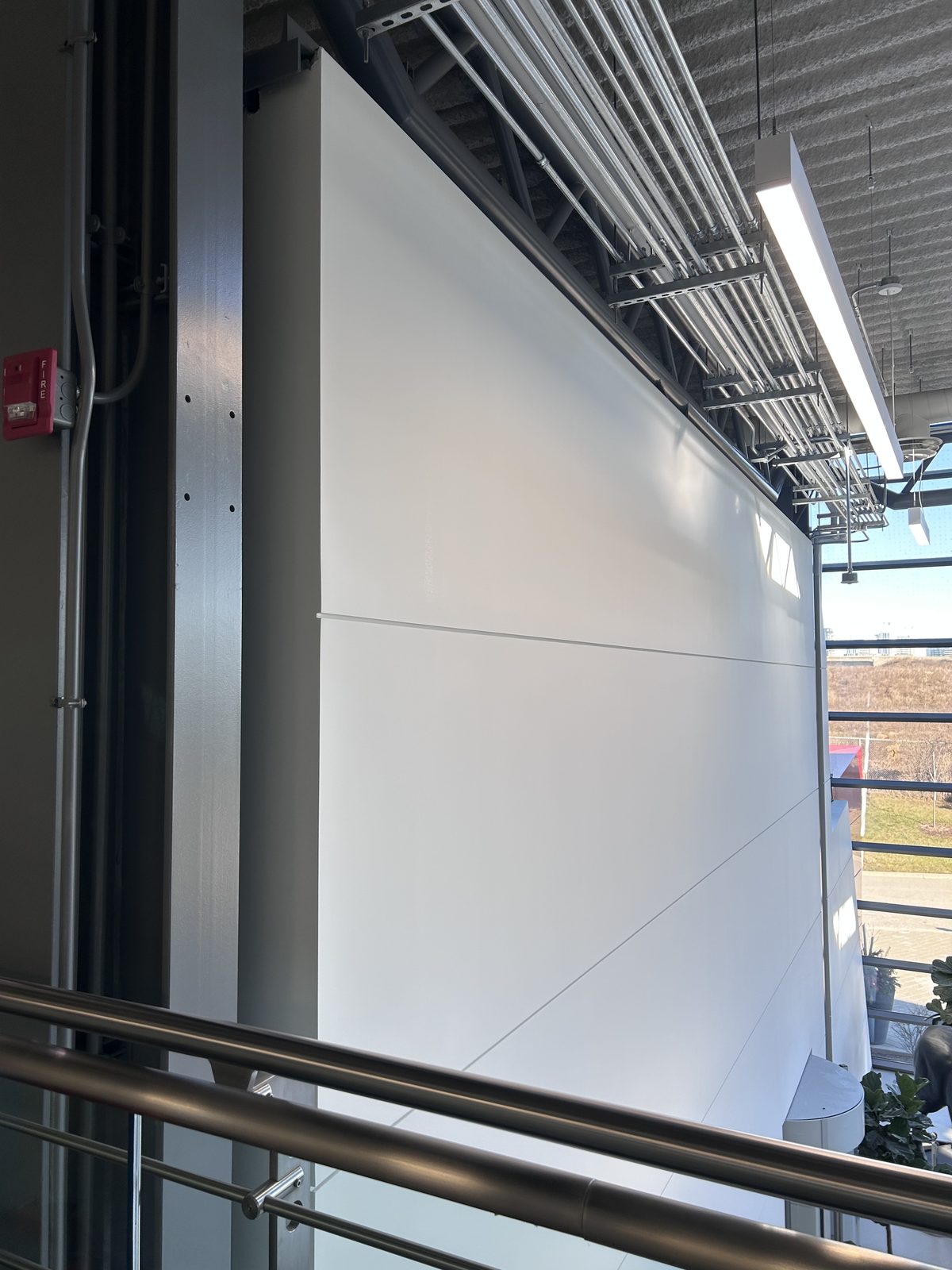 White painted feature wall seen from the mezzanine railing, with exposed ceiling and cable trays above