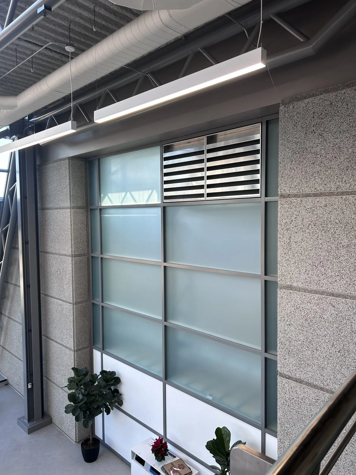 Mezzanine wall with frosted glass panels, a metal louvre and speckled stone-finish panels under pendant lights
