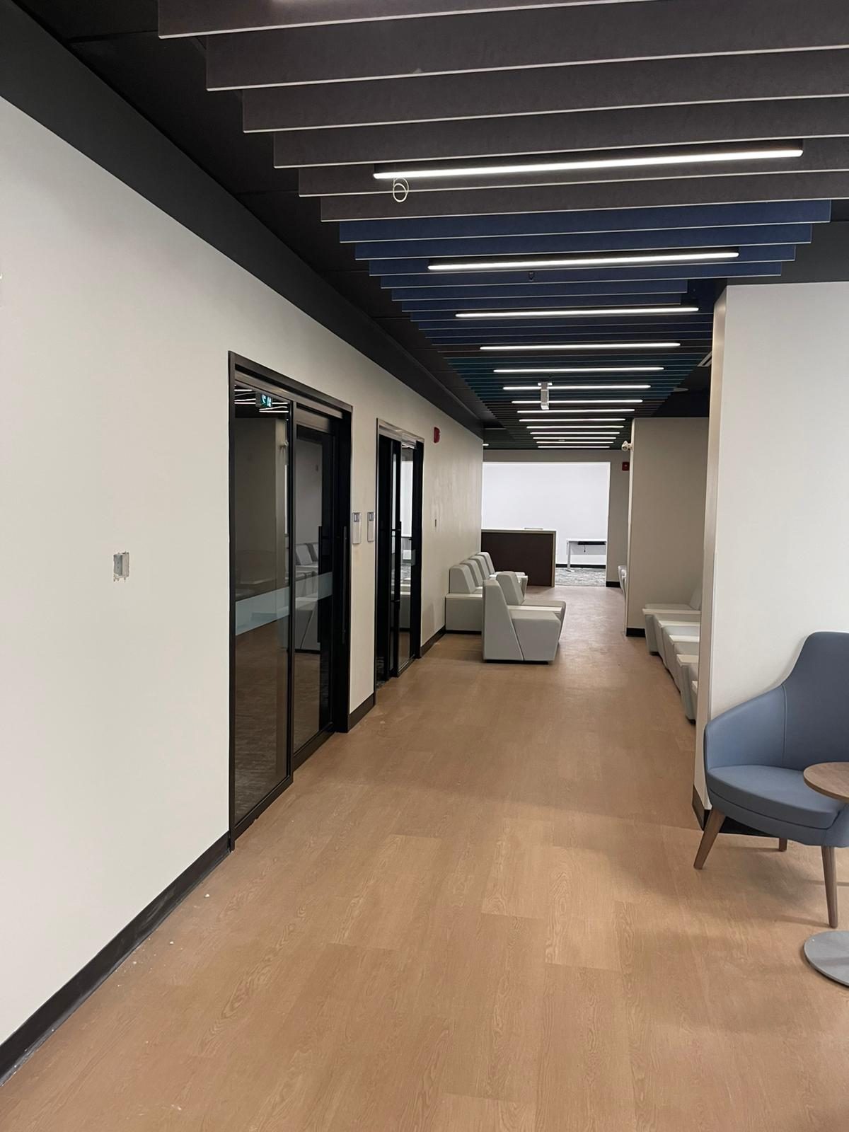 Corridor with white painted walls, black-framed glass doors and lounge seating in Building B at Georgian College in Barrie