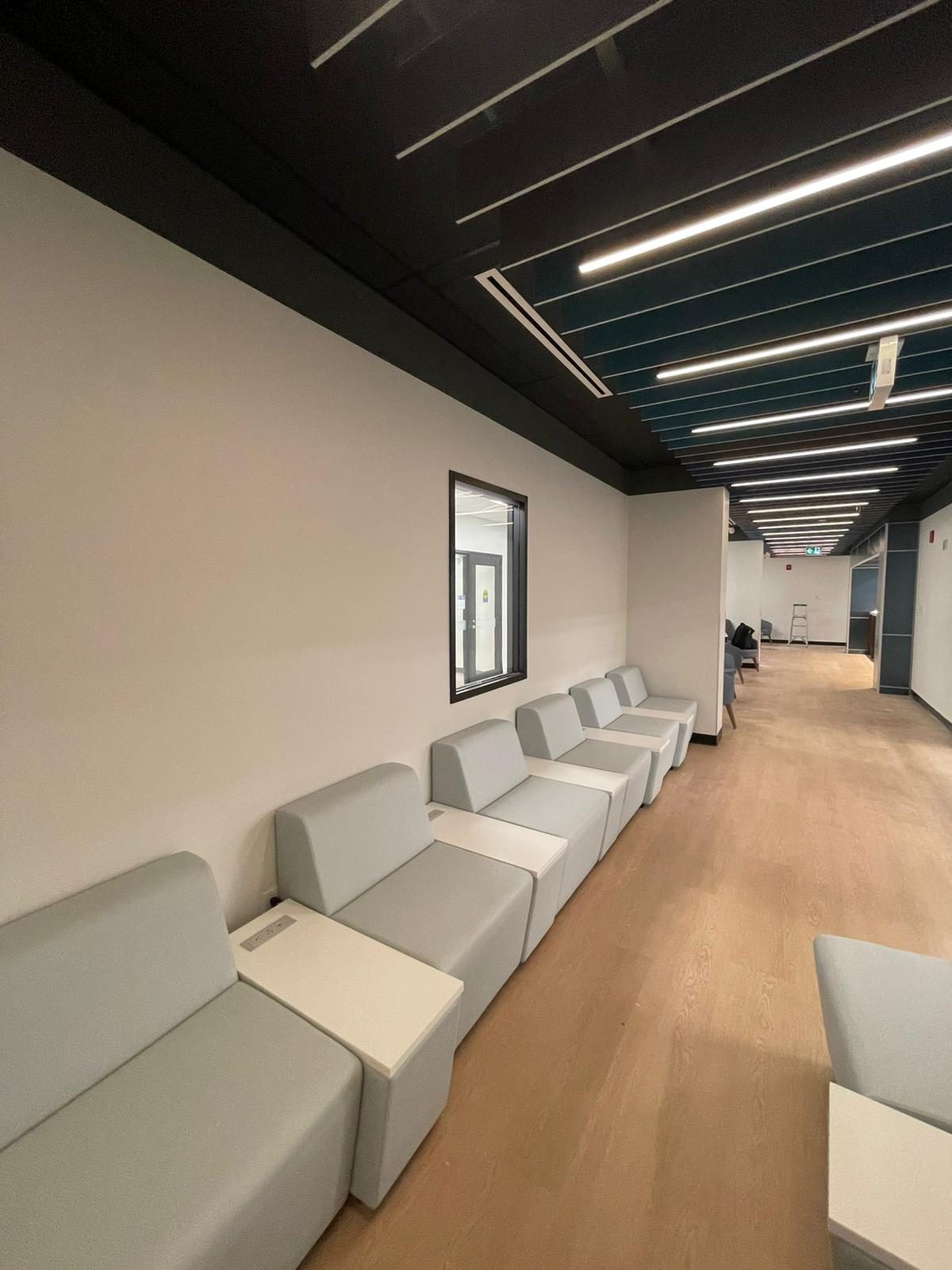 Lounge corridor with grey modular bench seating, white painted walls and a slatted ceiling with linear lights in Building B at Georgian College in Barrie