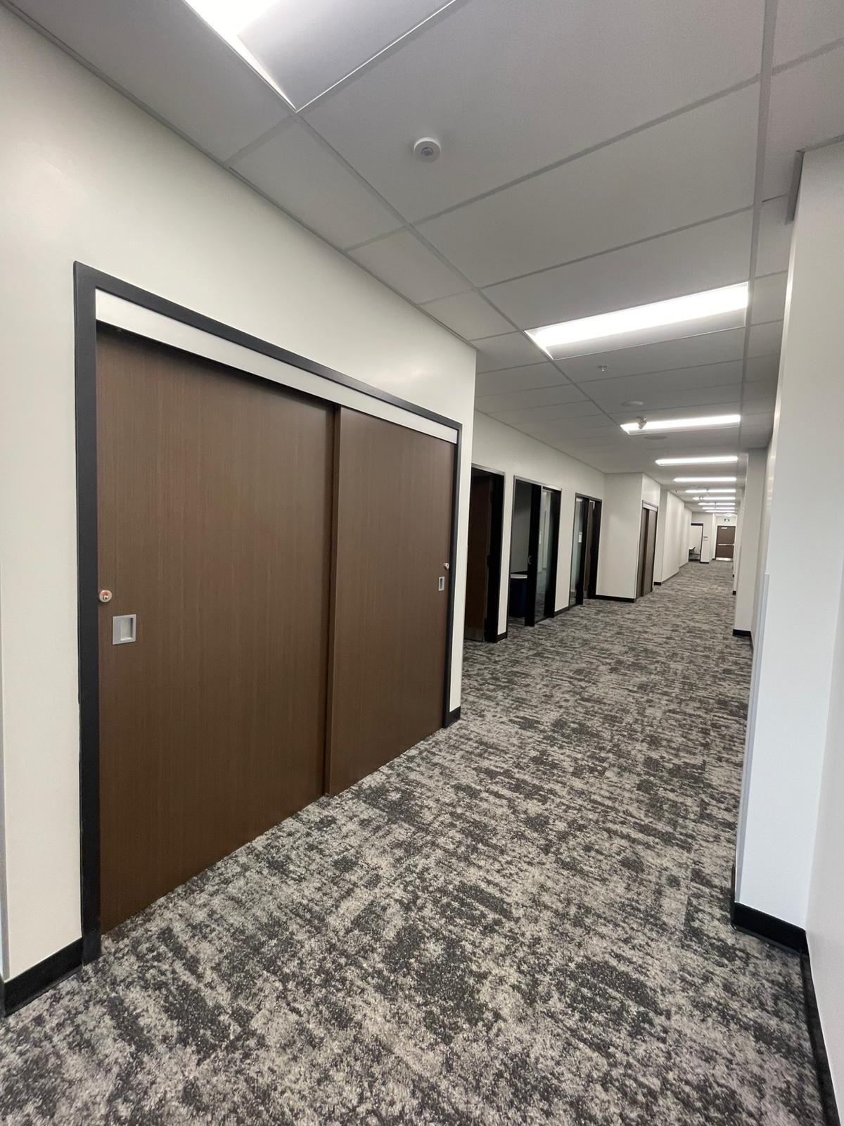 Carpeted office corridor with white painted walls and dark wood sliding doors in Building B at Georgian College in Barrie