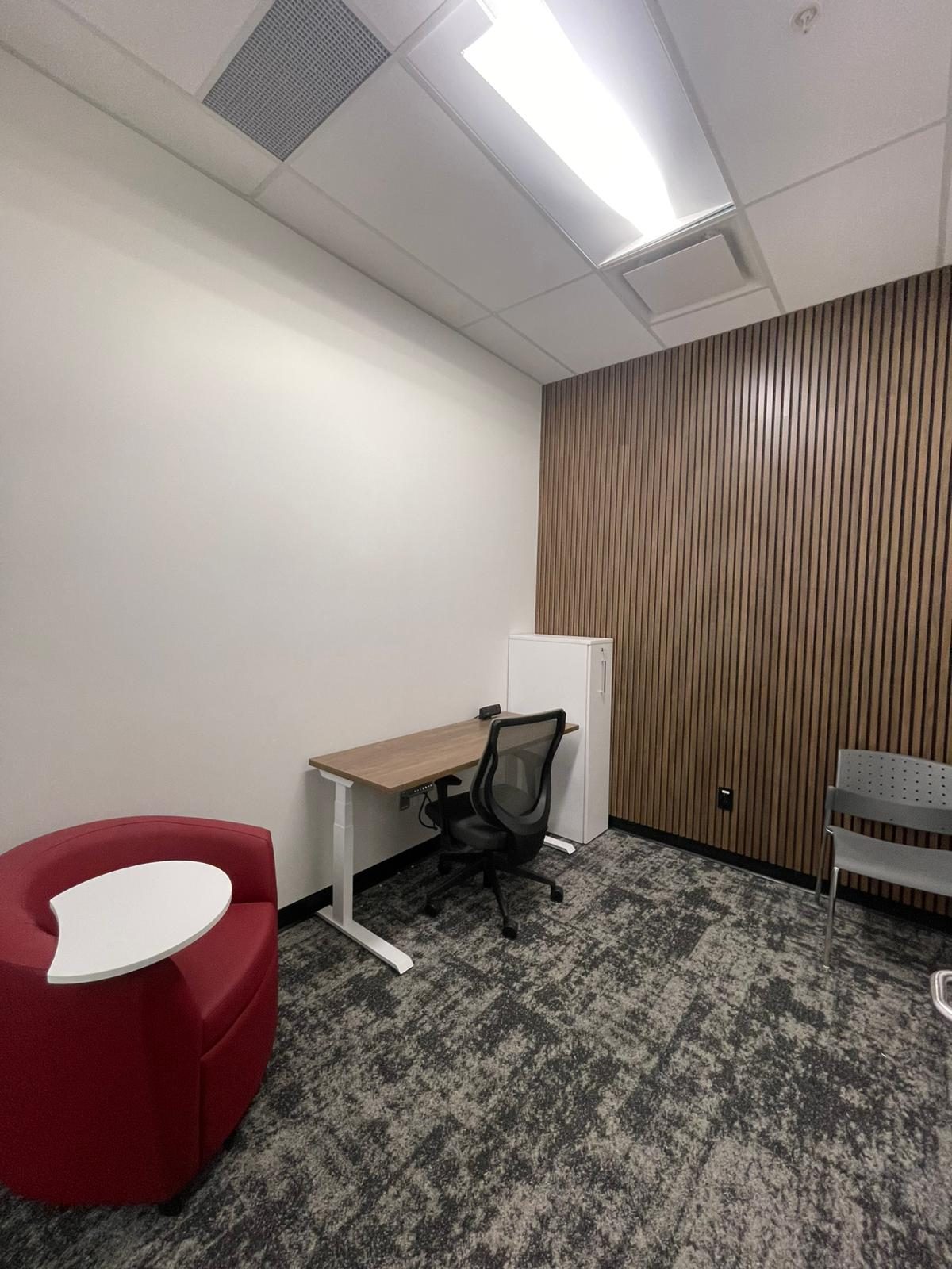 Private office with white painted walls, a wood slat feature wall and a sit-stand desk in Building B at Georgian College in Barrie