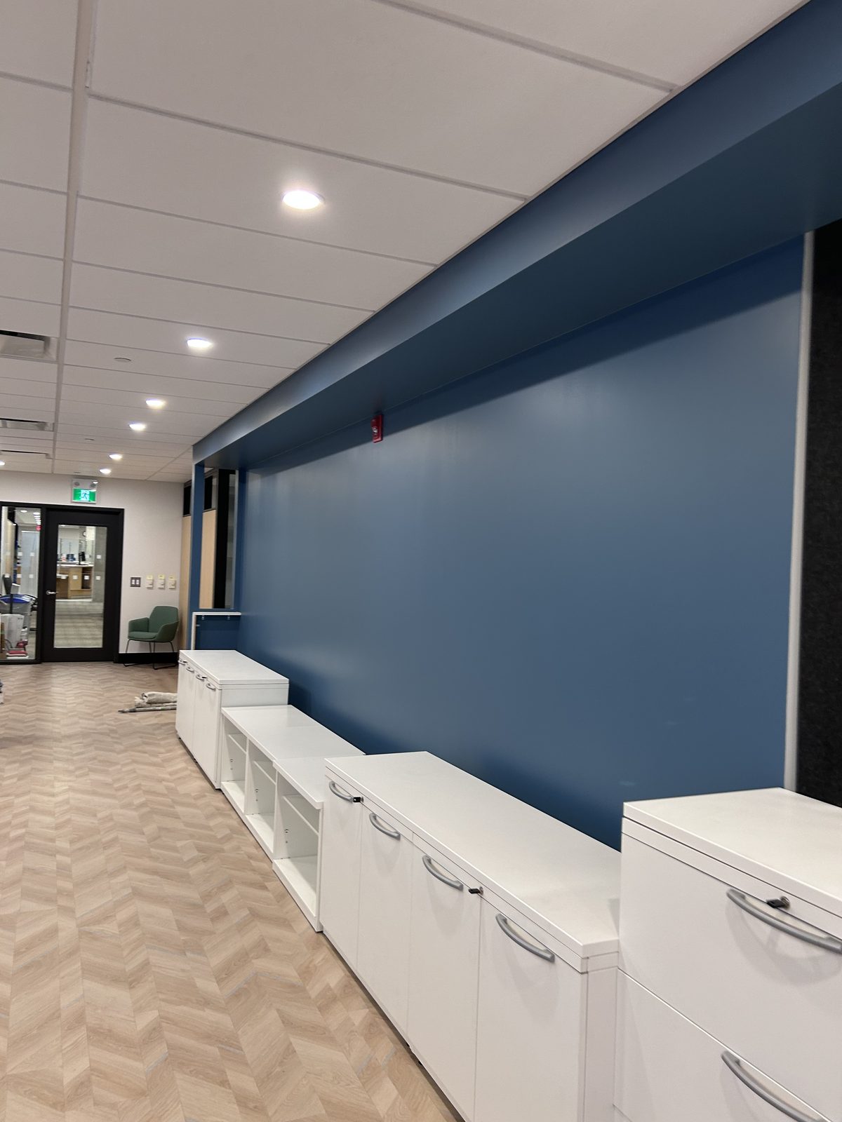 Corridor with a long blue painted wall and bulkhead above white storage cabinets and herringbone flooring