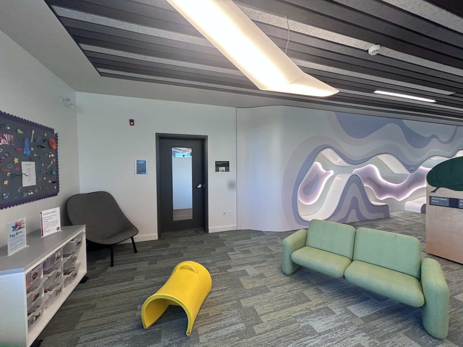 Children's area with a wavy illuminated wall feature, a green sofa and a door