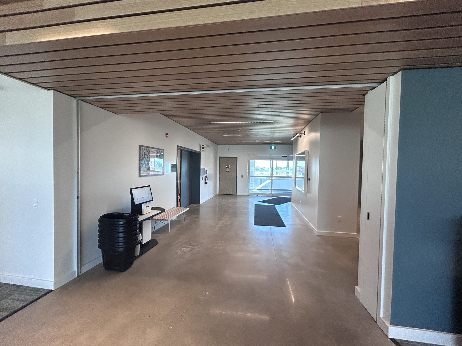 Entrance corridor with a wood slat ceiling, a self-checkout kiosk and an elevator