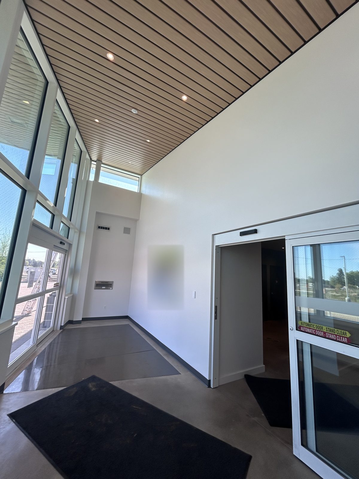 Entry vestibule with a sloped wood slat ceiling, white walls and an automatic sliding door