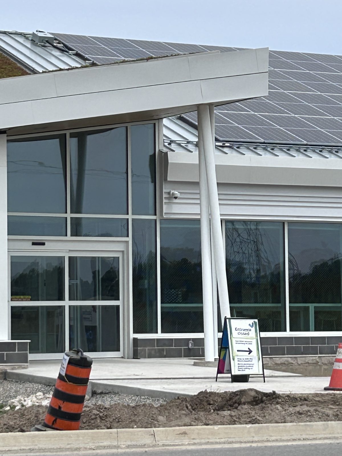 Exterior entrance with a glazed facade and roof-mounted solar panels while site work is still underway