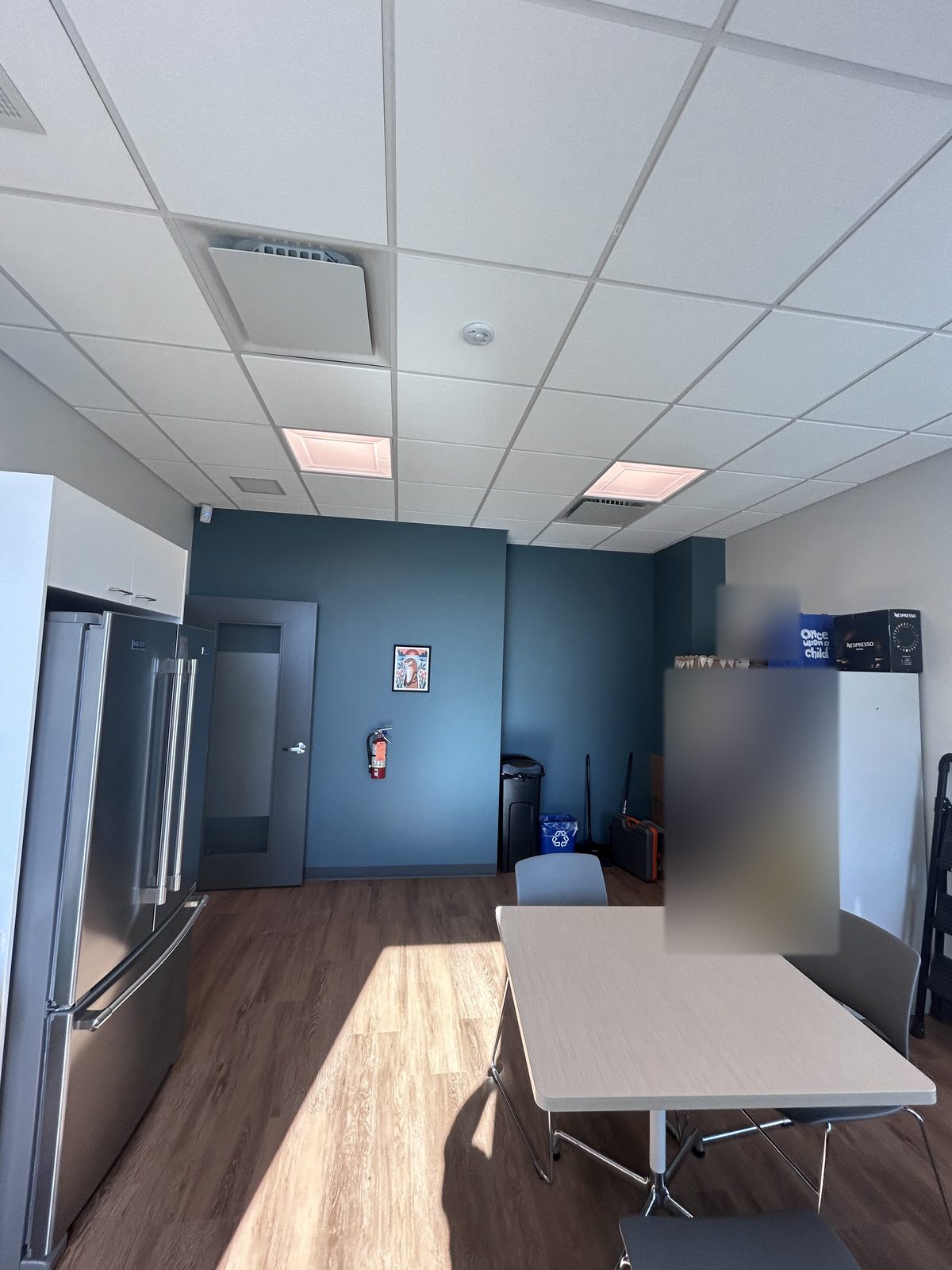 Room with a blue-grey accent wall, grey door, lockers, fridge and a table