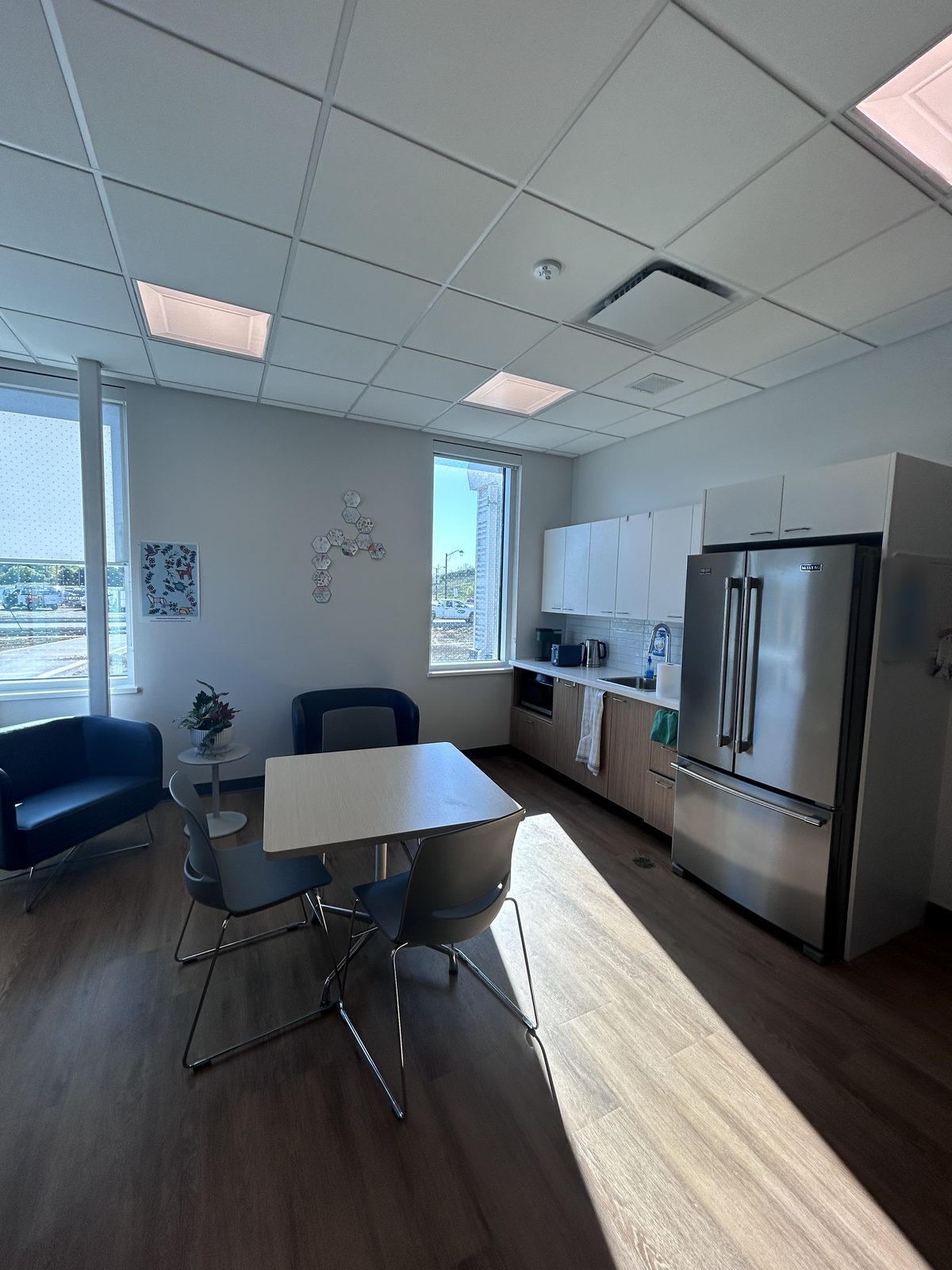 Kitchenette with white cabinets, a stainless steel fridge and blue armchairs