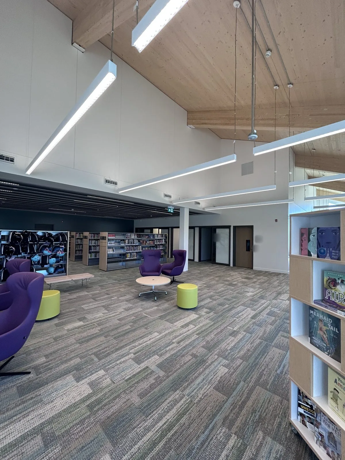 Open reading area with purple lounge chairs, book stacks, white painted walls and dark-framed doors