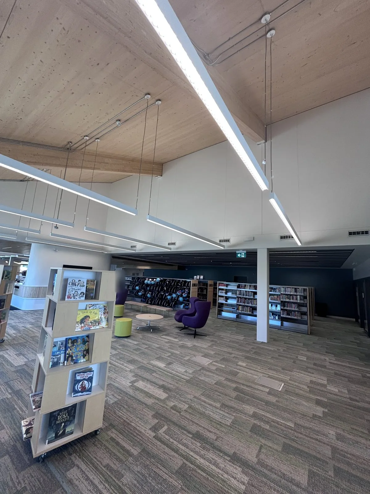 Reading area with a book display tower, round column, curved slatted desk and green ottomans