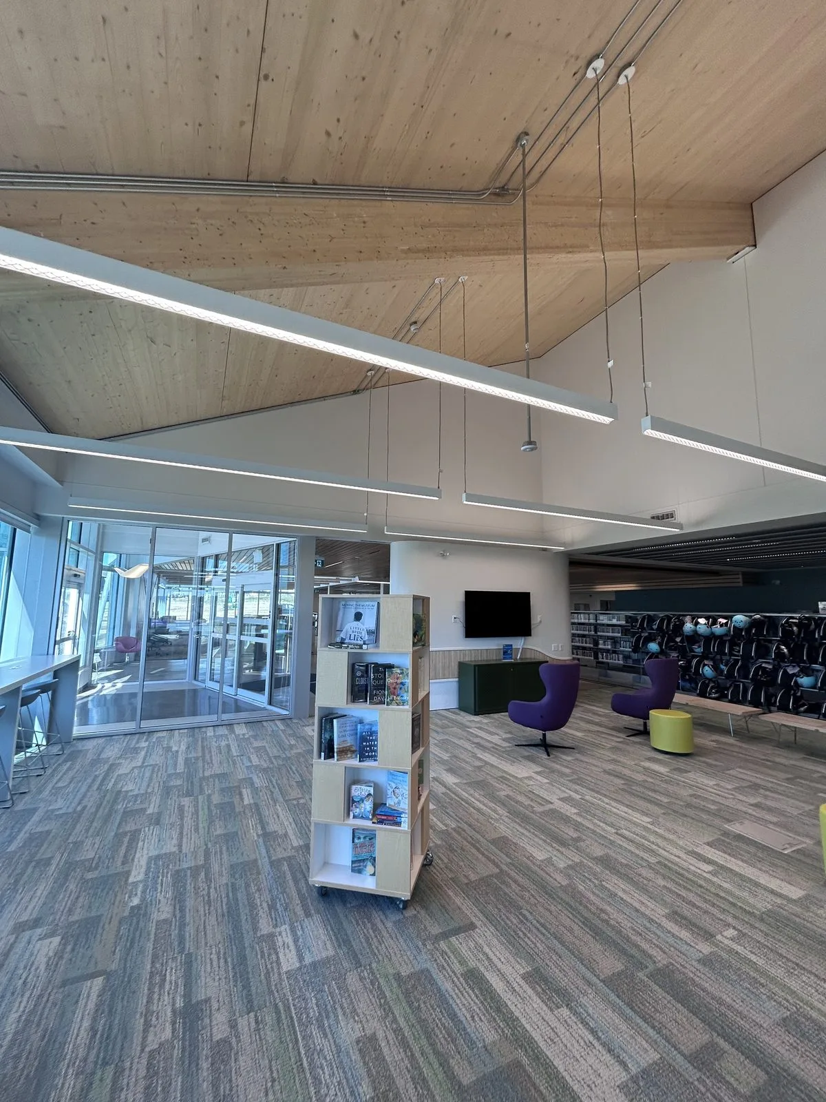 Open area with purple chairs, a book display tower and a glass entrance vestibule