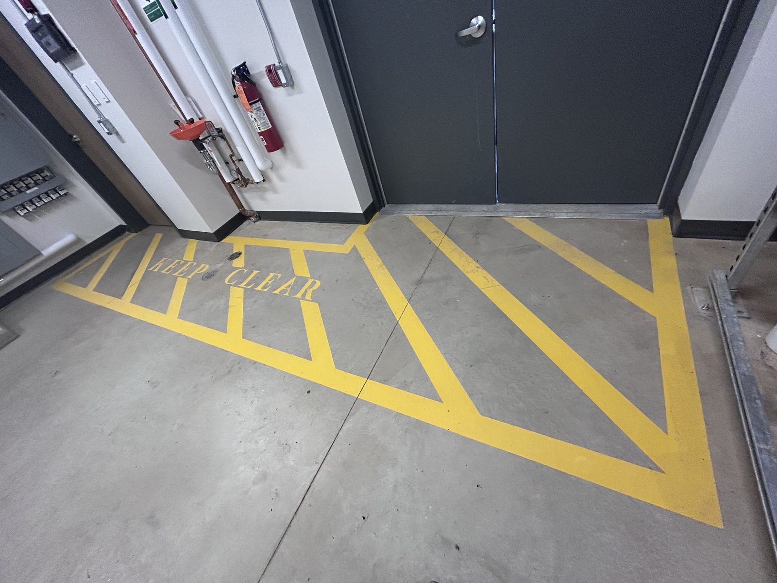 Service room with grey double doors, yellow Keep Clear floor markings, a fire extinguisher and an eyewash station
