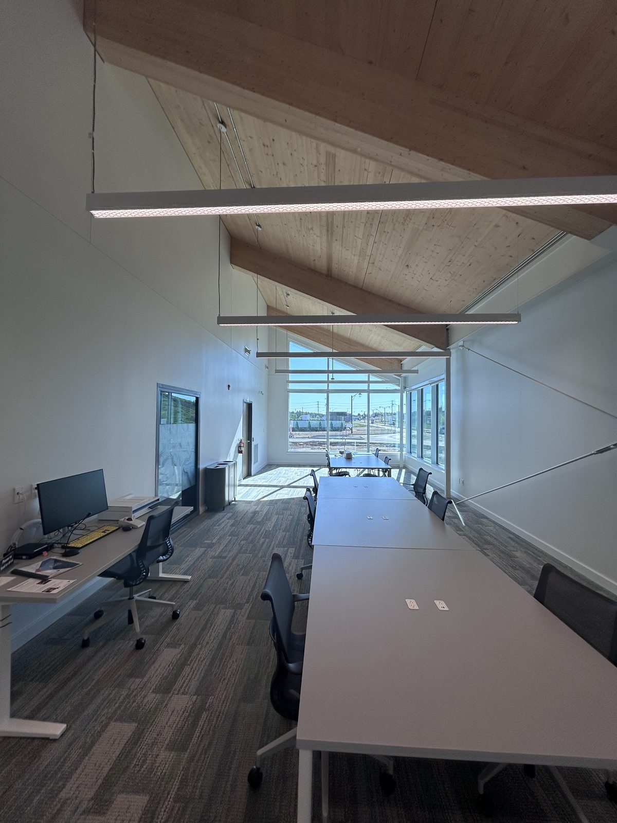 Study room with an exposed timber ceiling, long tables, white walls and a full-height window wall