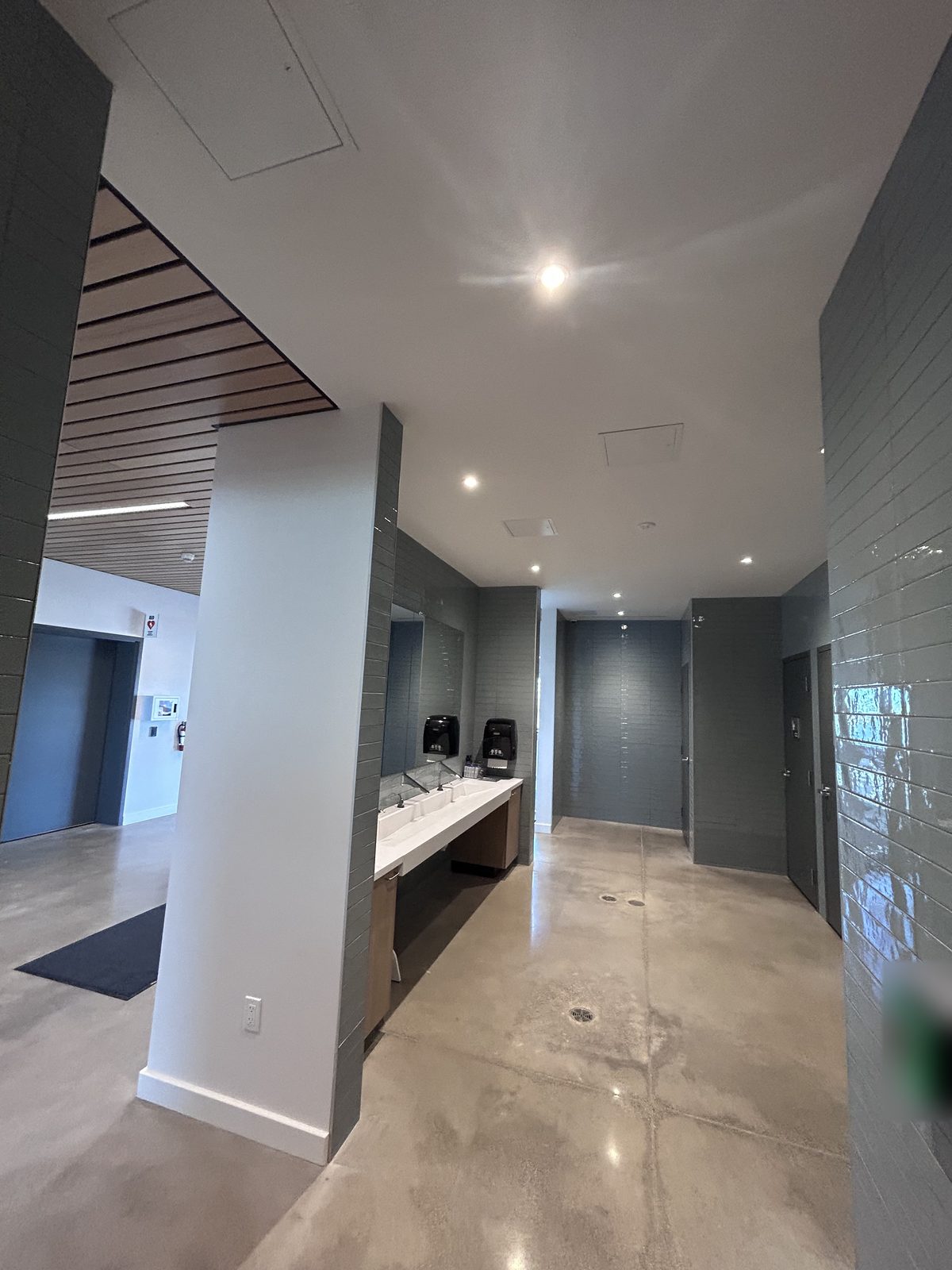 Washroom vestibule with grey tile walls and a trough sink