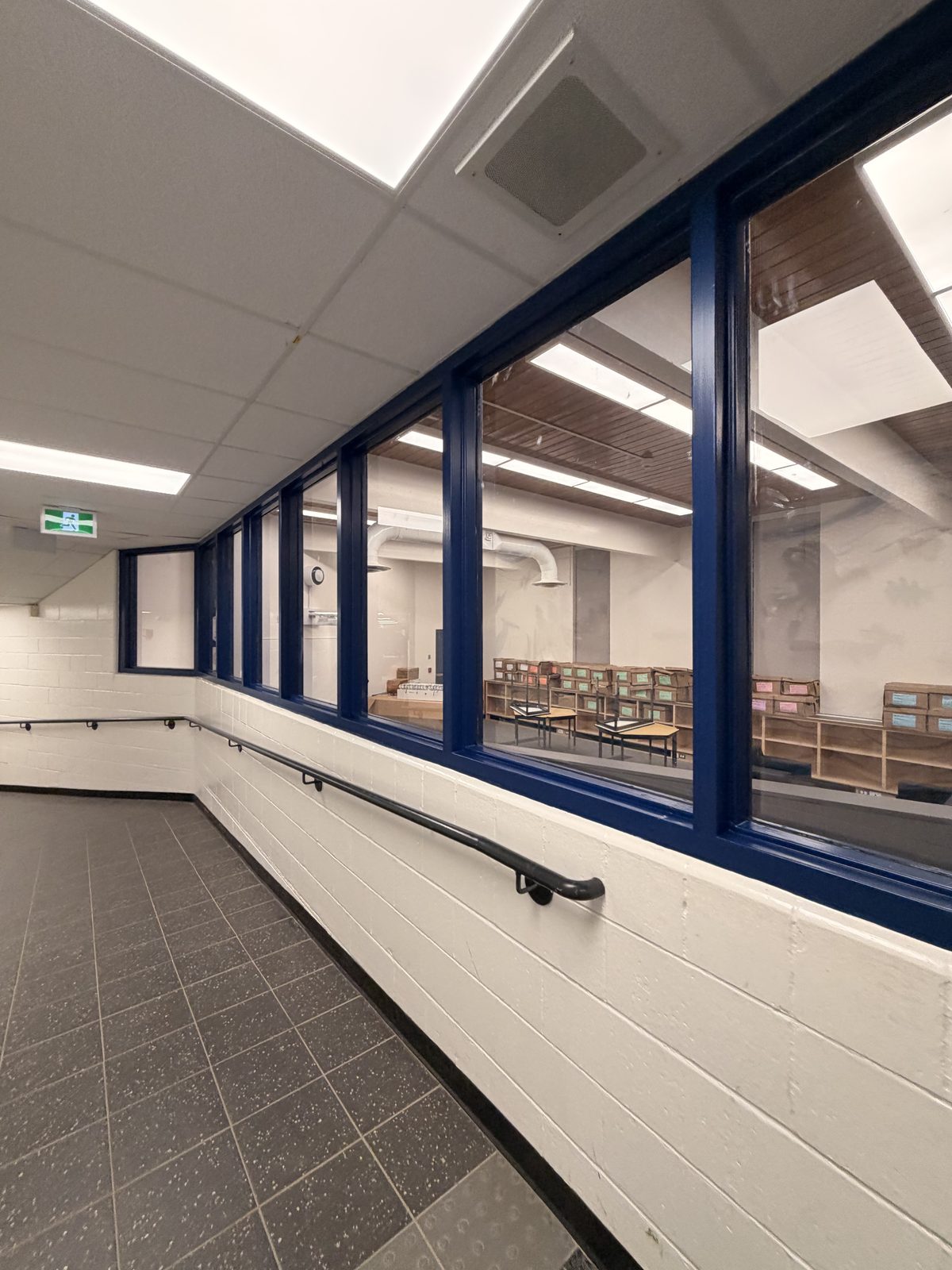 Corridor with dark blue painted window frames, white painted block walls and a black handrail at Roseneath Centennial School in Roseneath