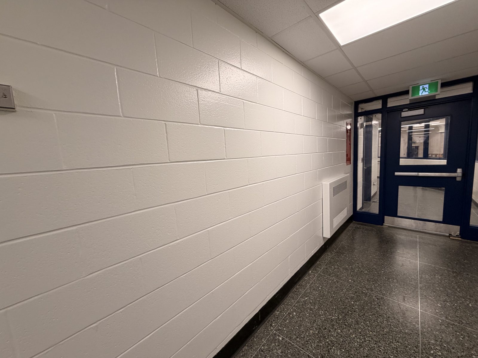 Corridor with a white painted block wall leading to a dark blue painted door and frame at Roseneath Centennial School in Roseneath